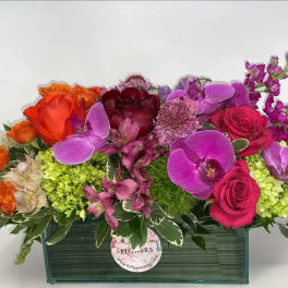 Mixed bouquet of roses, orchids, and purple blooms in a rectangular vase