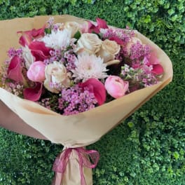 Bouquet of pink and cream flowers wrapped in tan paper with a ribbon