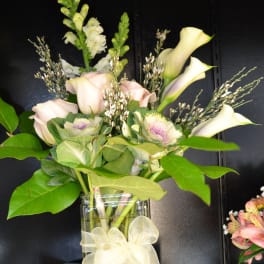 Bouquet of pale roses and calla lilies in a glass vase with a ribbon bow