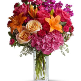 Bright mixed bouquet of pink hydrangea, roses, and orange lilies in a tall glass vase