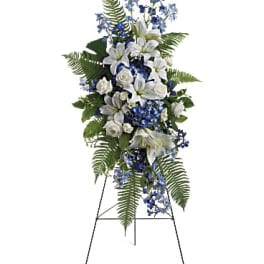 Standing floral spray with white lilies, roses, and blue flowers on an easel
