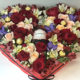 Heart-shaped flower box with roses, orchids, and chocolates around a bottle of wine