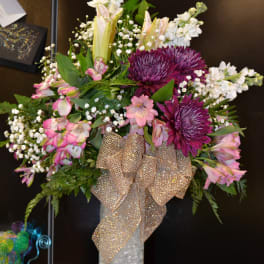 Bouquet of purple and pink flowers in a glass vase with a gold ribbon