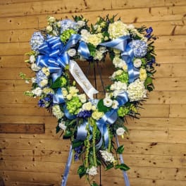 Heart-shaped floral wreath with blue ribbons on a stand