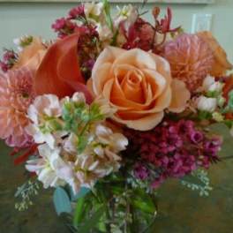 Peach roses and dahlias with pink accent flowers arranged in a clear glass vase
