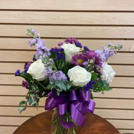 Bouquet of white roses and purple flowers in a glass vase with a purple ribbon
