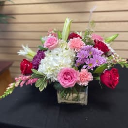 Mixed pink, white, and purple flower arrangement in a square glass vase