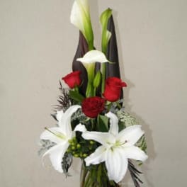 Tall bouquet of white calla lilies, white lilies, and red roses in a glass vase