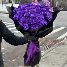 Large bouquet of purple roses wrapped in black paper with a purple ribbon