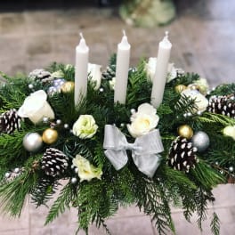 Holiday centerpiece with white candles, roses, pinecones, and a silver bow