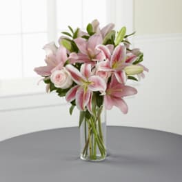 Pink lilies and roses arranged in a clear glass vase