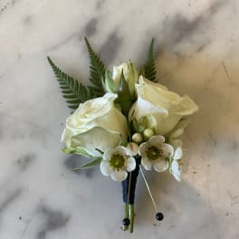 White rose boutonniere with small white accent flowers and fern fronds