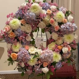 Large pastel floral wreath on a stand with roses, hydrangeas, and mums
