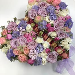 Pastel bouquet of roses, lavender blooms, and macarons tied with a lilac ribbon