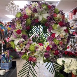 Large floral wreath with lilies, roses, and purple blooms on a stand