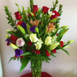 Tall mixed bouquet of roses, lilies, and orchids in a clear glass vase