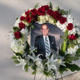Floral funeral wreath with red roses and white lilies around a framed portrait