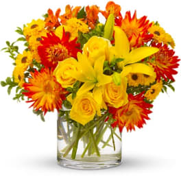 Yellow roses and lilies in a clear glass vase with red and orange flowers