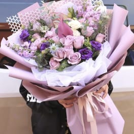 Large bouquet of pink and purple flowers wrapped in pastel paper