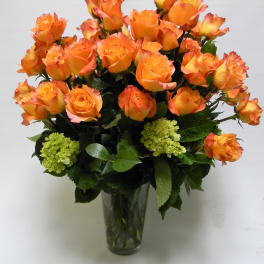 Orange roses arranged in a clear glass vase with green hydrangea accents