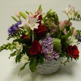 Mixed bouquet of roses, lilies, and hydrangea in a white basket