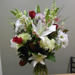 Tall mixed bouquet with red roses, white lilies, and white daisies in a glass vase