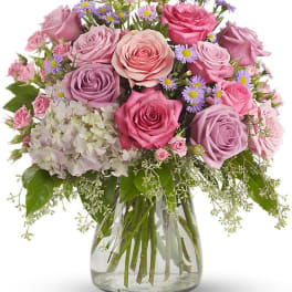 Pink and lavender roses arranged in a clear glass vase with small purple daisies