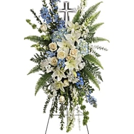 Standing funeral spray with white lilies, cream roses, and blue flowers on an easel