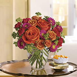 Orange roses and magenta daisies in a clear glass vase