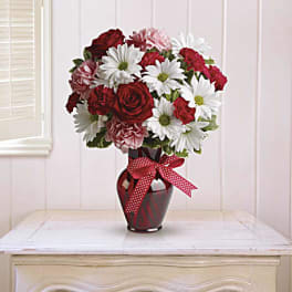 Bouquet of red roses, white daisies, and pink carnations in a red vase