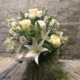 White and cream floral arrangement with lilies and roses in a glass vase