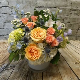 Mixed bouquet of peach roses, hydrangeas, and blue thistle in a white vase