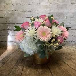 Pink roses and gerbera daisies in a gold vase with white hydrangea