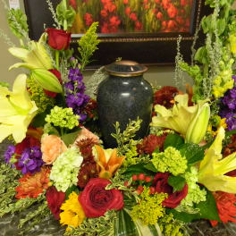 Colorful floral arrangement surrounding a dark urn on a table