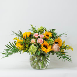 Low round arrangement of yellow sunflowers and pink roses in a clear glass bowl vase