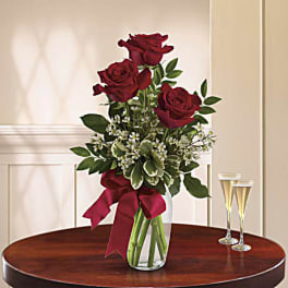 Three red roses in a glass vase with a burgundy ribbon