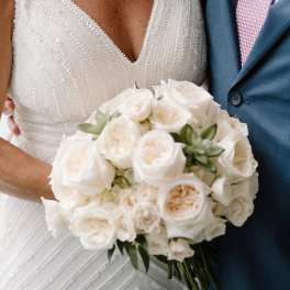 Bride holding a white rose bouquet beside a man in a blue suit