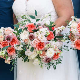 Bride and bridesmaids holding coral and blush rose bouquets