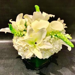 White lilies and hydrangeas arranged in a low vase with green accents