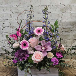 Pink and purple floral arrangement in a white wooden box with a butterfly accent