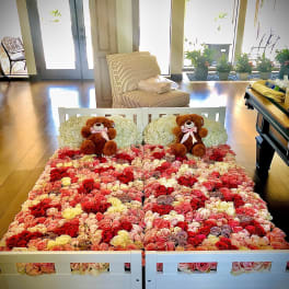 Bed covered in multicolored roses with two teddy bears at the headboard