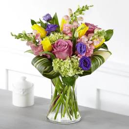 Mixed bouquet of pink, purple, and yellow flowers in a clear glass vase