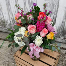 Mixed bouquet of pink, white, yellow, and purple flowers in a glass vase with a pink ribbon