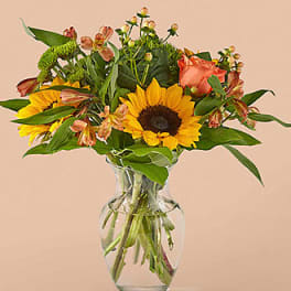 Sunflowers and peach roses arranged in a clear glass vase