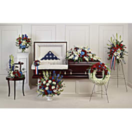 Patriotic funeral floral tributes around a casket with red, white, and blue flowers