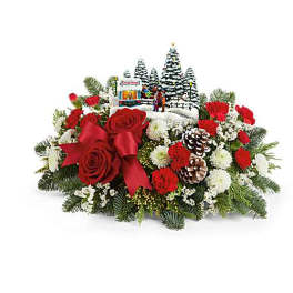 Christmas floral arrangement with red roses, pinecones, and a small winter village scene