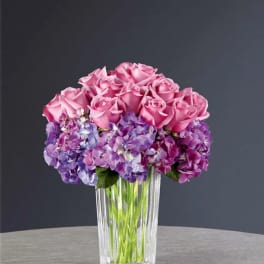 Pink roses and purple hydrangeas arranged in a clear glass vase.