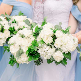 Bridesmaids holding white rose bouquets with greenery