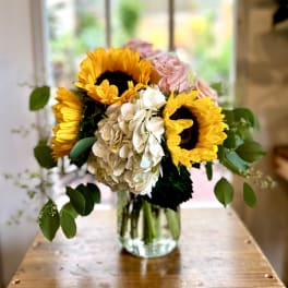 Bouquet of sunflowers, hydrangea, and pink roses in a glass vase