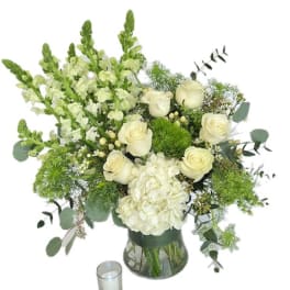 White roses and hydrangea in a glass vase with a small candle